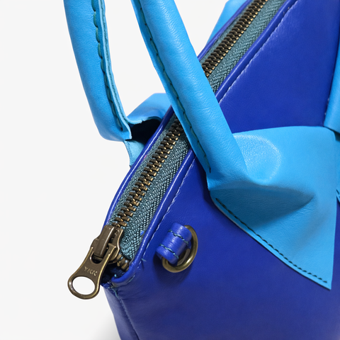 Close-up of brass zipper and sky blue rolled handle on royal blue lambskin crossbody