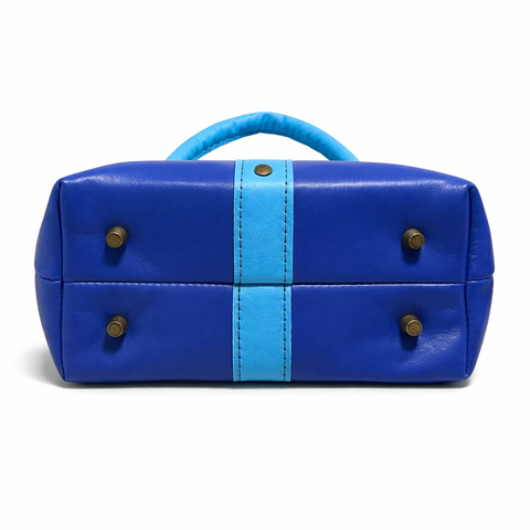 Bottom of royal blue crossbody bag showing 4 brass purse feet and sky blue center stripe