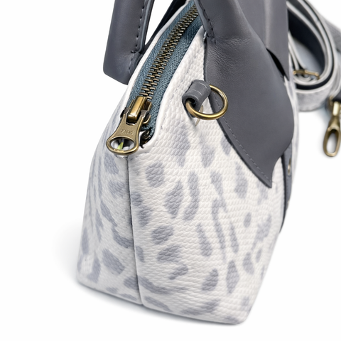 Close-up side view of white python print leather bag showing snake embossed texture and gray lambskin collar detail with brass hardware