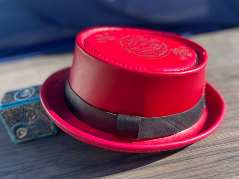 Red leather pork pie hat with a black hat band and a custom laser engraved image on the top of the hat