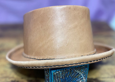 natural leather pork pie hat with black hand stitching against a purple backdrop