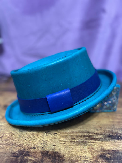 Turquoise leather hat with a blue hat band and black hand stitching against a purple backdrop