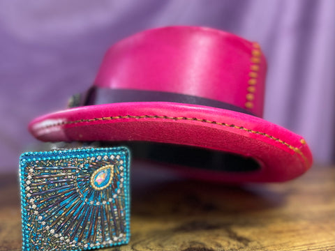 Back of a Pink Leather Pork Pie Hat with a purple hat band with a jewel and light brown hand stitching against a purple backdrop