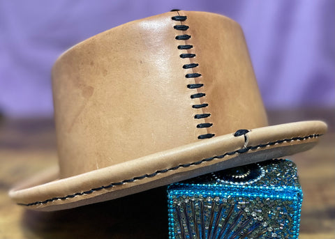back of a natural colored leather pork pie hat with black hand stitching against a purple backdrop