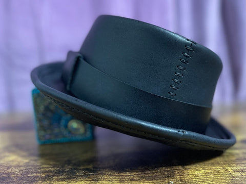 Back of a black leather pork pie hat and hand stitching with a purple back drop