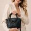 Woman holding an emerald teal handbag with a collar design against a beige background