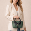 Woman holding a green handbag against a beige background