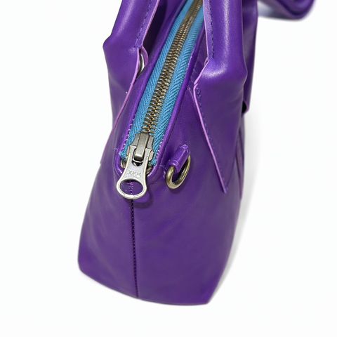 Close-up of YKK antique brass zipper pull and D-ring hardware on handmade royal purple lambskin leather bag