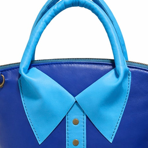 Close up of a royal Blue handbag with a sky blue collar and button detail on a white background
