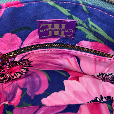 Interior of royal purple lambskin collar bag showing navy and pink floral cotton lining, interior zipper pocket, and embossed Inspired Leather Co. brand label
