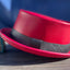 Red leather pork pie hat with a black hat band against a blue backdrop