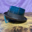 Back of Leather Pork Pie Hat with visible hand stitching that is turquoise at the top and brown at the bottom against a purple backdrop