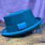 Turquoise leather pork pie hat with black hand stitching against a purple backdrop