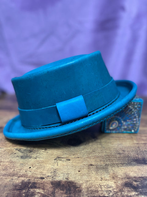 Turquoise leather pork pie hat with black hand stitching against a purple backdrop