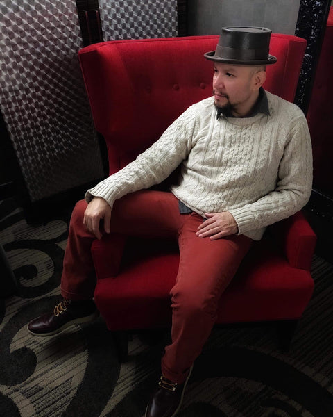 Man wearing a dark brown leather pork pie hat while seated in a large red chair