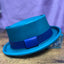 Turquoise leather hat with a blue hat band and black hand stitching against a purple backdrop