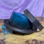 Leather Pork Pie Hat that is turquoise at the top and brown at the bottom against a purple backdrop