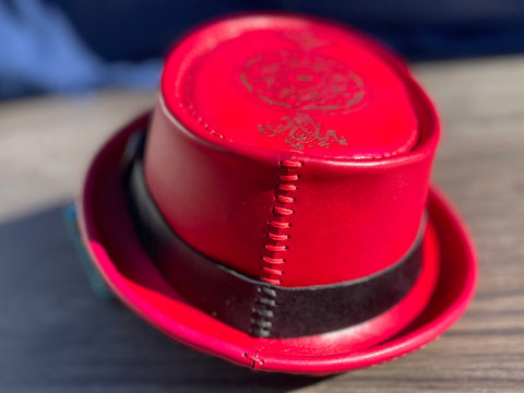Back of a red leather pork pie hat with hand stitching and a custom laser engraved image on the top of the hat.